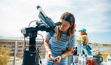 A student looks in a telescope at the sun from a roof deck.